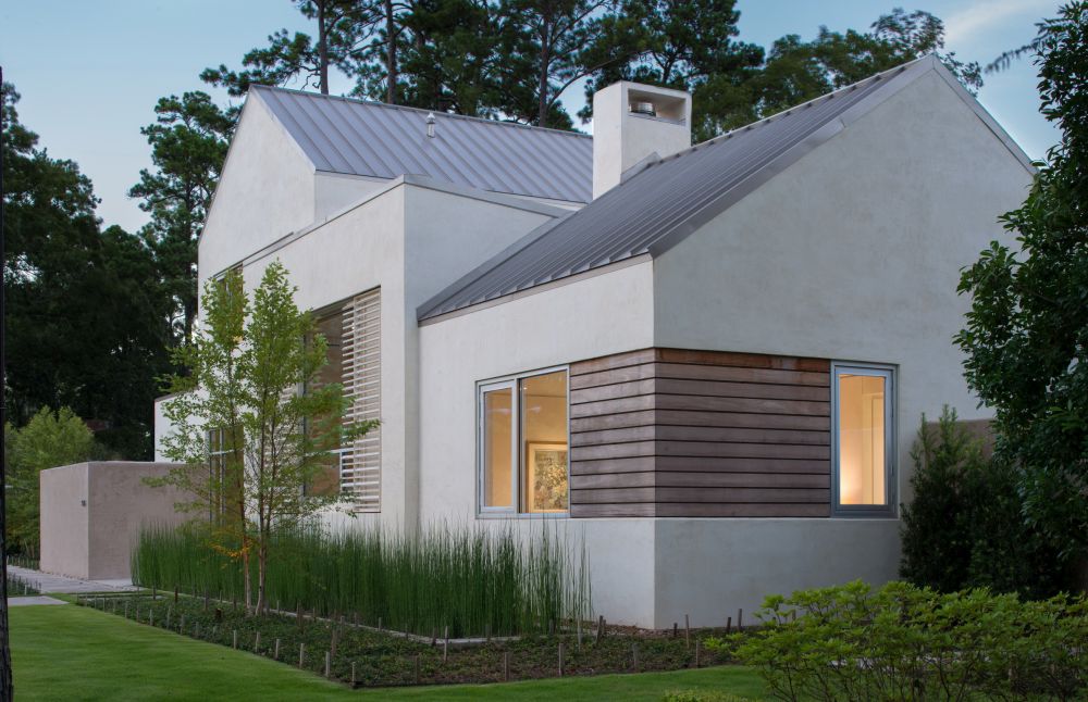 Linear garapa wood window accents coordinate with the custom metal shutters beyond, standing seam metal roof above, and the horsetail reed landscaping across the front.